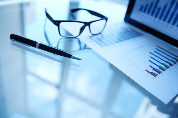 Image of paper, eyeglasses, pen and electronic data in touchpad on workplace